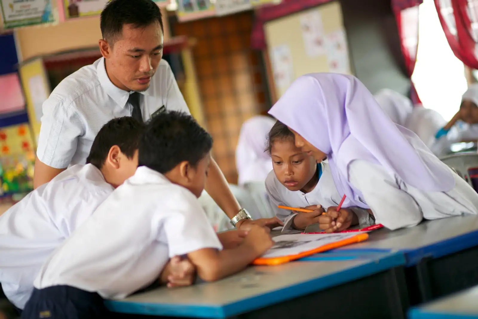 A teacher guiding pupils as they work together at a classroom table in SK Pulau Indah, Port Klang