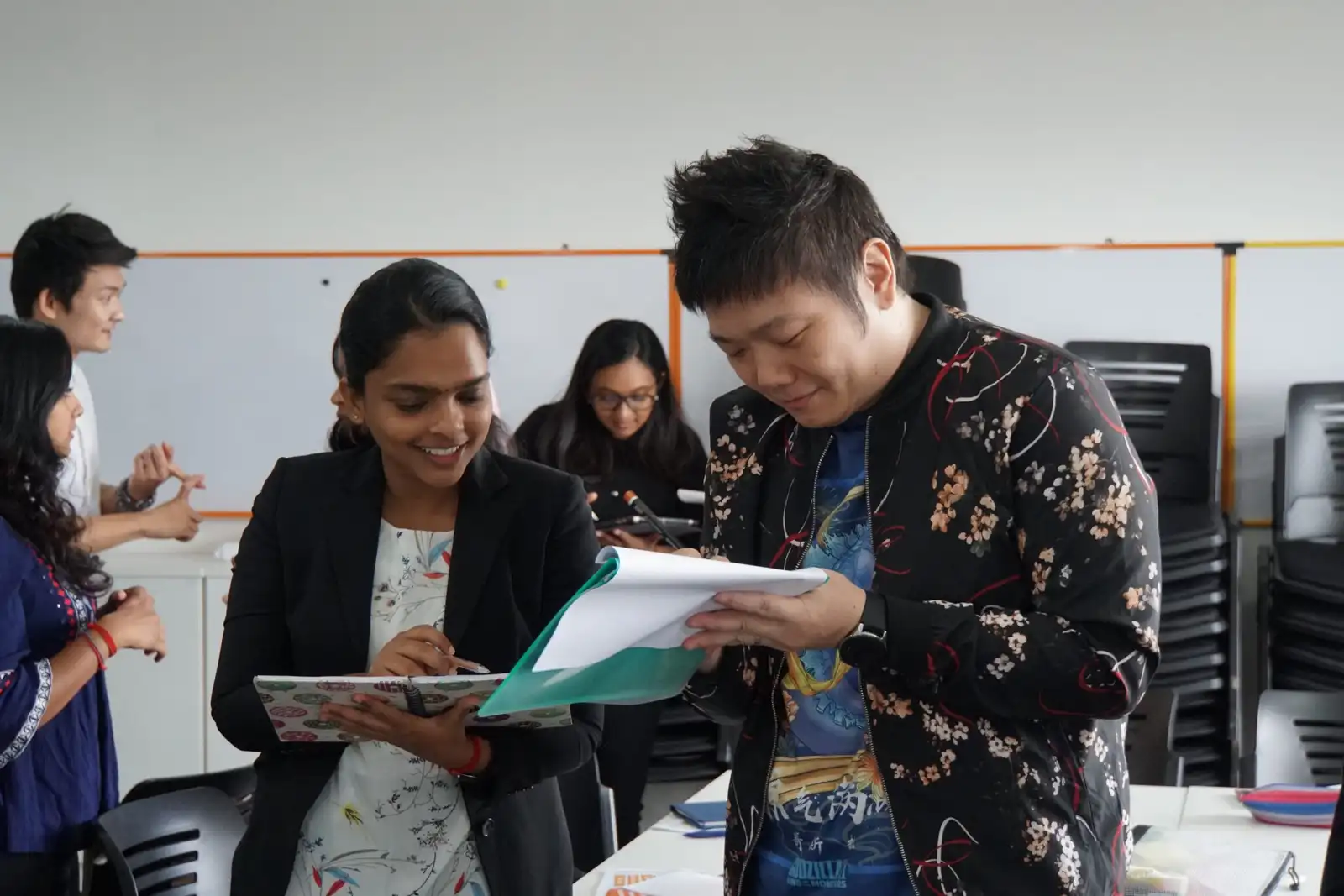 Two teachers smiling as they compare notes during a training workshop